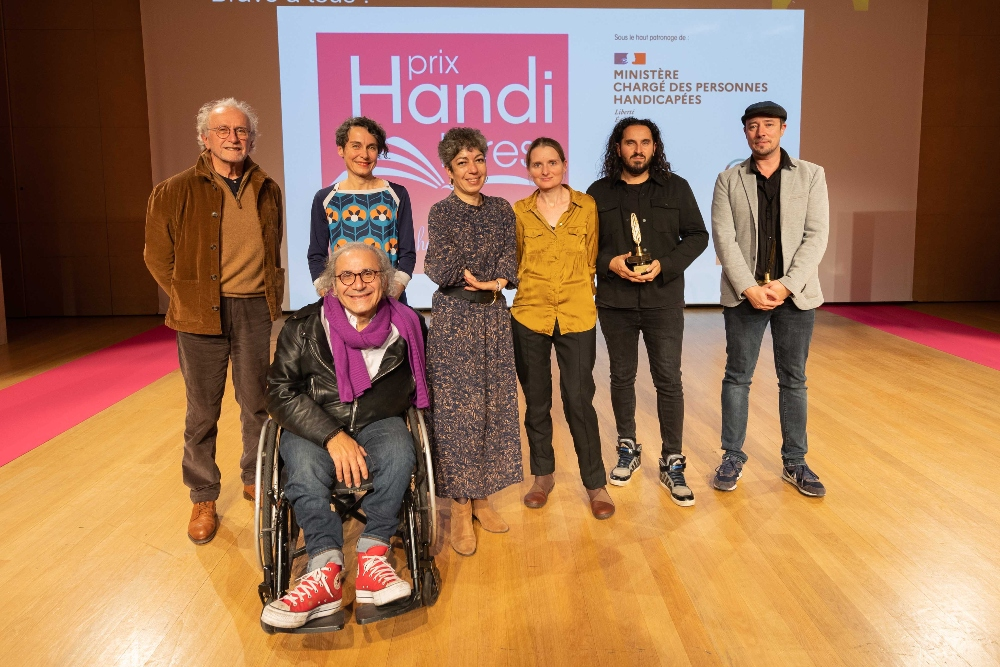 Photo d'un groupe de 7 personnes devant l'affiche du prix Handi Livres