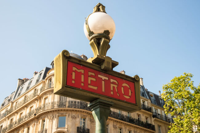 Paris, France. August 2022. Traditional Paris metro sign with buildings in the background Illustration du signe traditionnel de métro parisien, en sortie d'une station au cœur de Paris