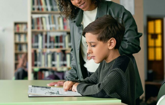 Un écolier lit une page d'un manuel scolaire avec l'aide de sa maitresse