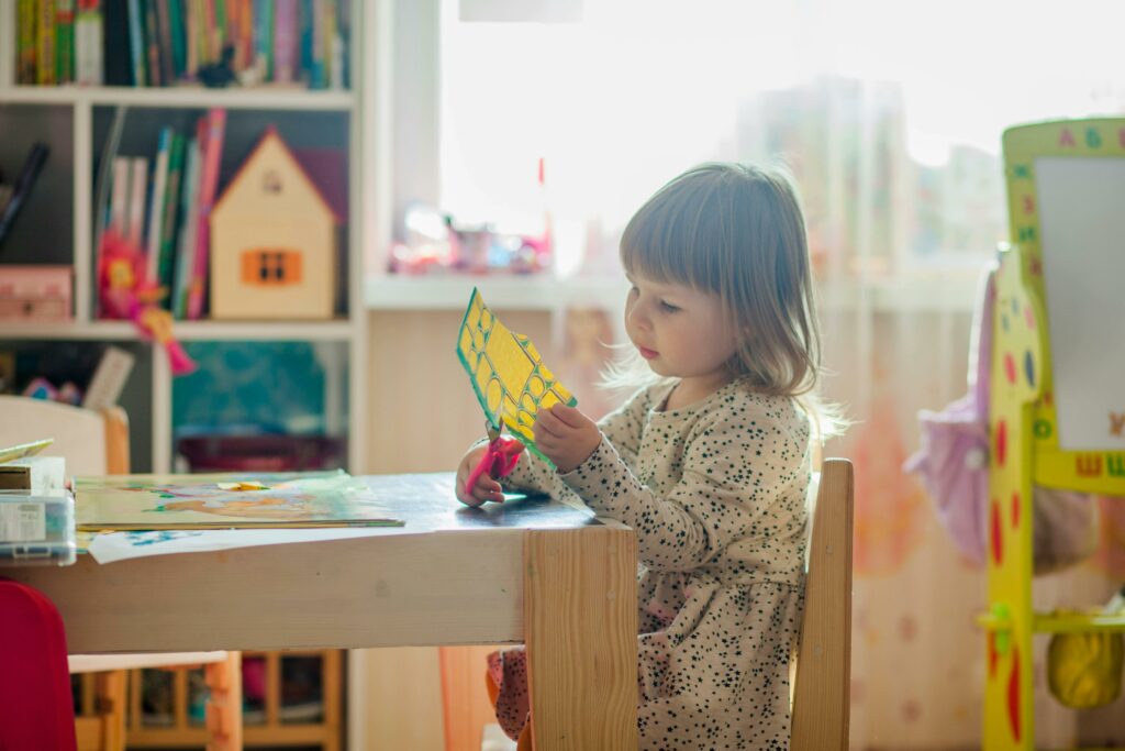 Une enfant d'école maternelle fait du découpage assise à une table