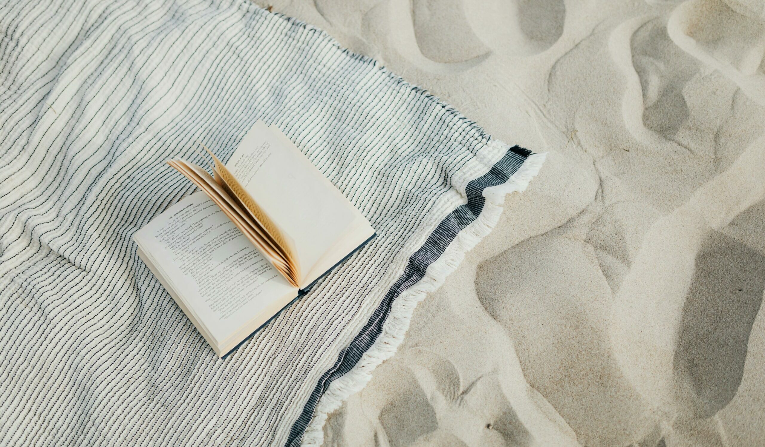 Un livre ouvert posé sur une serviette de plage sur du sable fin