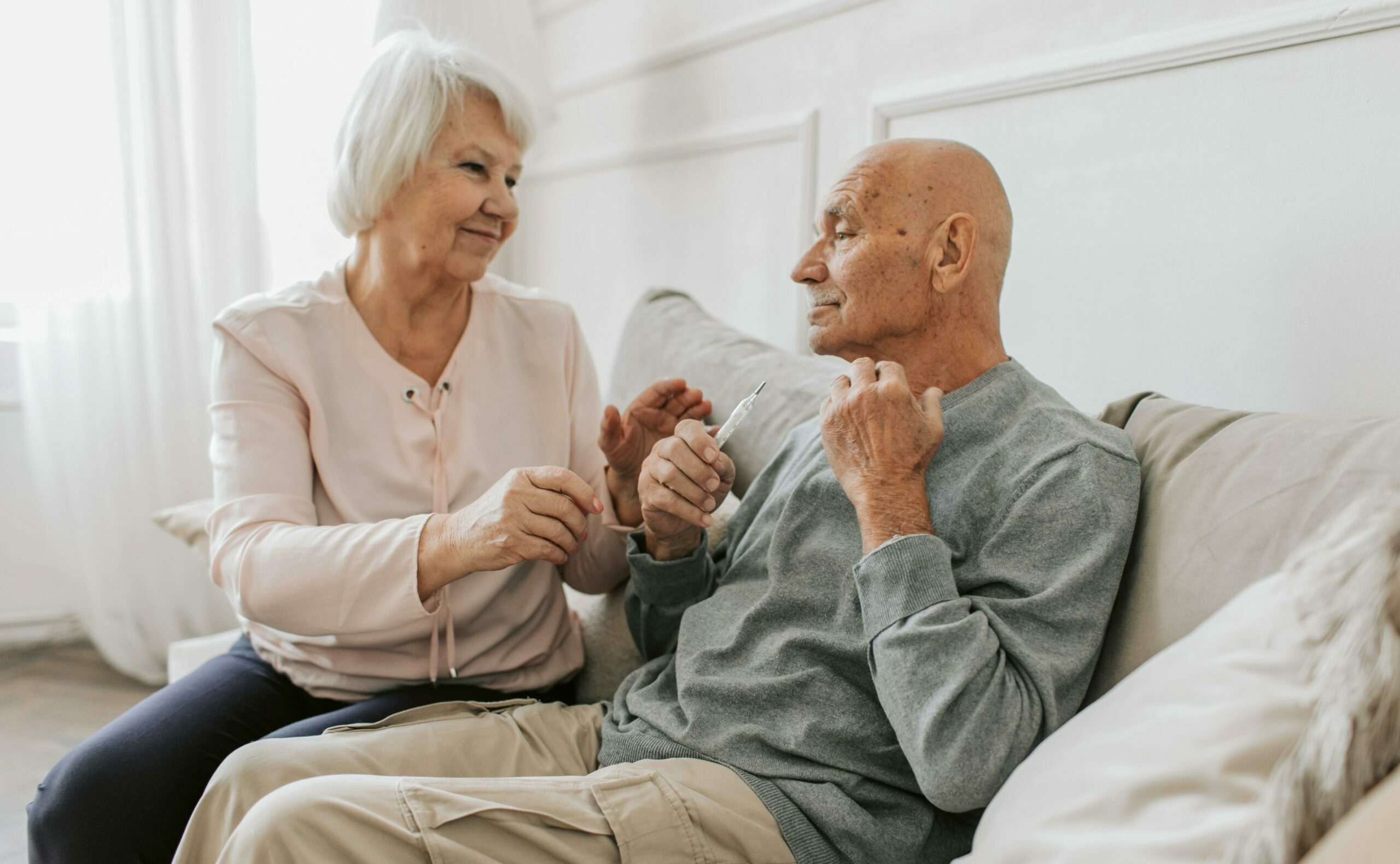 Un homme en perte d'autonomie assis dans un canapé reçoit le soutien de son épouse proche aidante