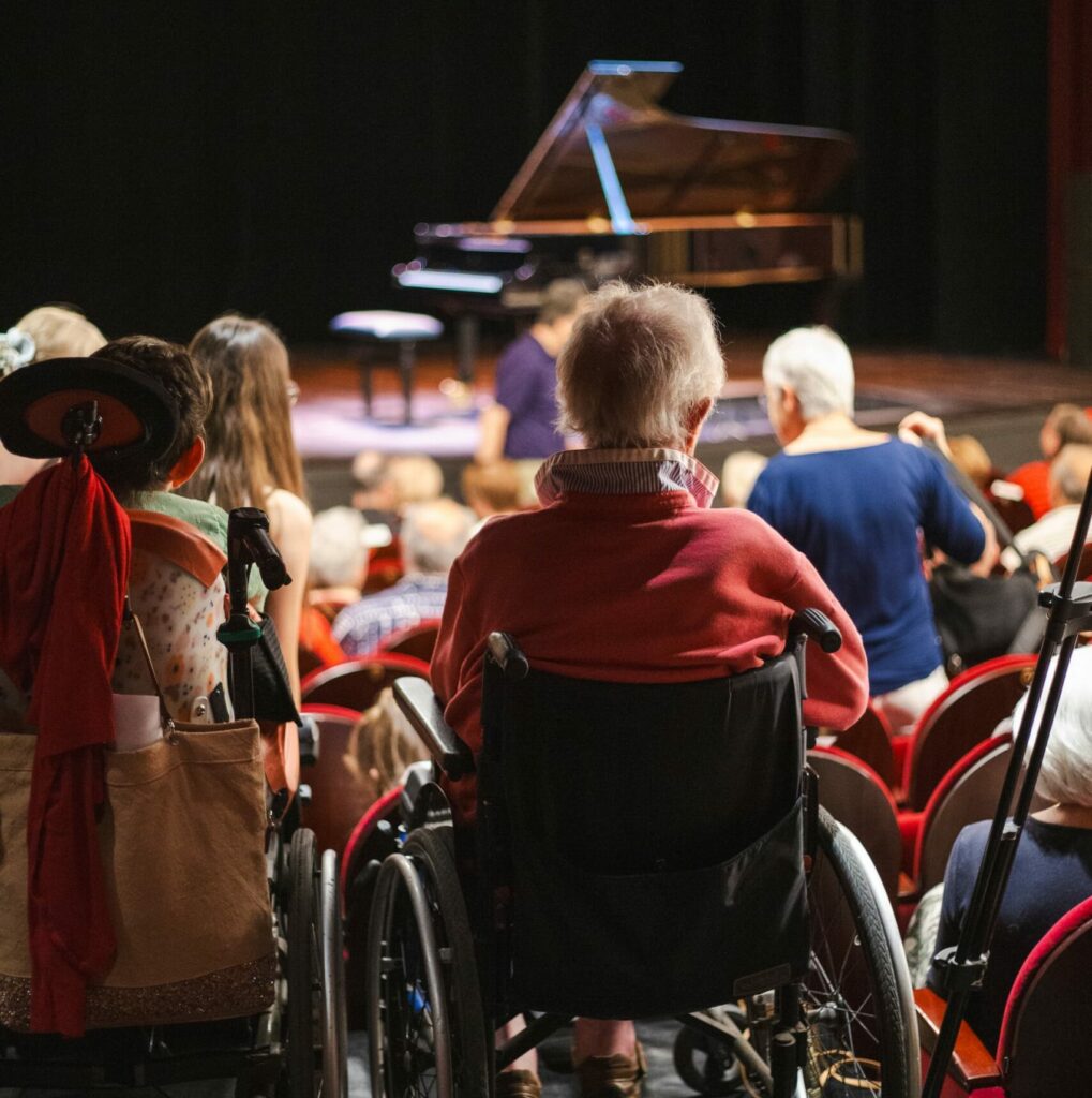 Une personne en chaise roulante dans un auditorium avant un concert de l'Offrande Musicale