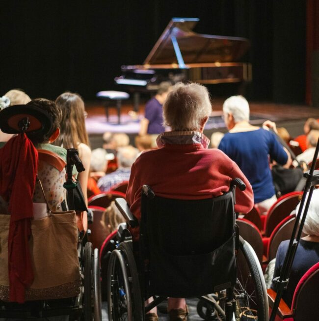 Une personne en chaise roulante dans un auditorium avant un concert de l'Offrande Musicale