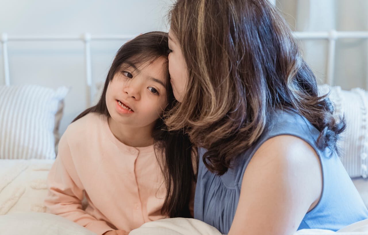 Une maman embrasse sur le front sa jeune fille handicapée