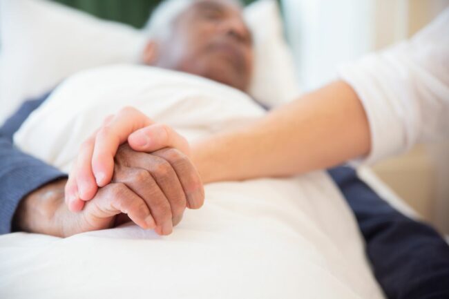 personne-agée-malade-main-aidant Un aidant tient la main d'un homme âgé alité