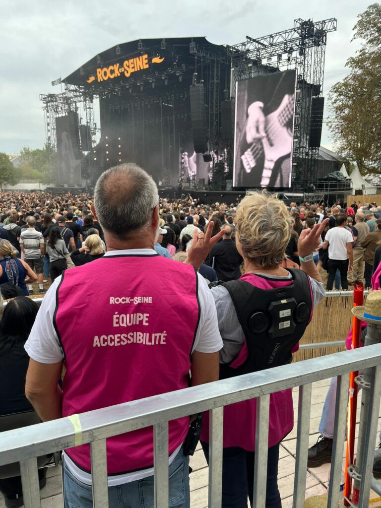 Deux membres de l'Equipe Accessibilité lors de Rock en Seine 2026. A droite, la femme porte un gilet vibrant.